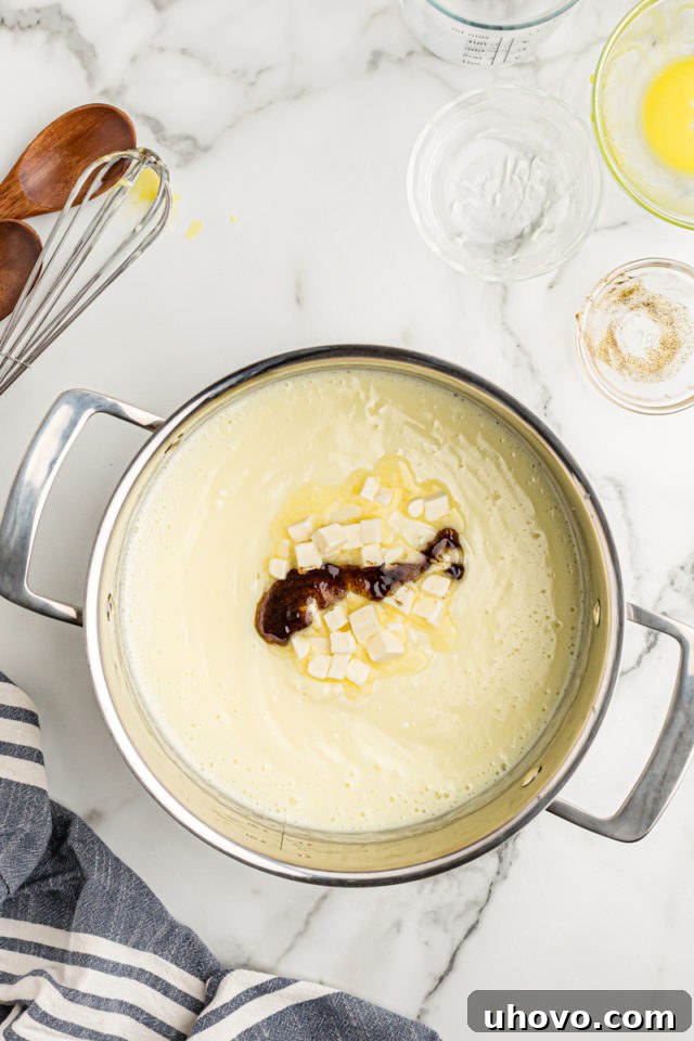 Adding small pieces of butter and a generous pour of vanilla extract to a pan of freshly cooked vanilla pudding, ready for the final stir.