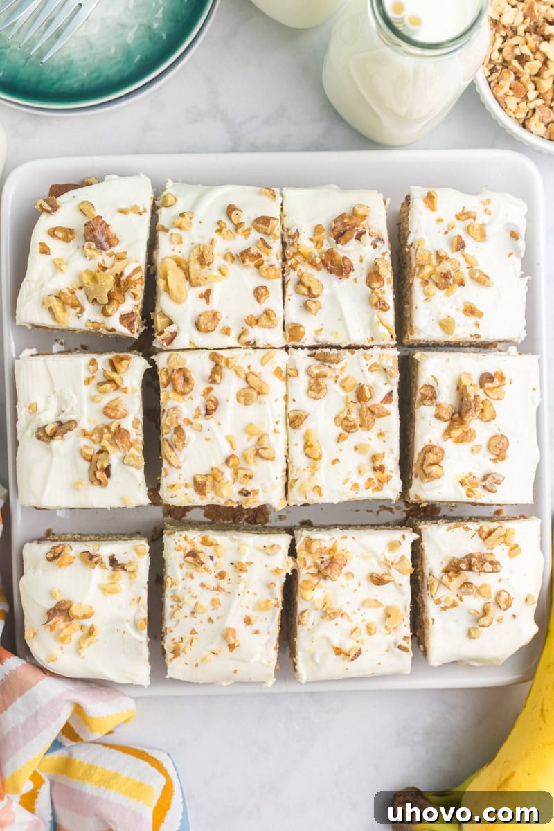 An overhead view of a freshly baked and frosted banana cake, neatly sliced into squares and arranged on a elegant square white serving plate.