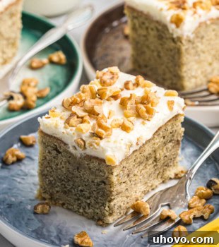 A slice of banana cake with cream cheese frosting on a blue plate with more servings in the background