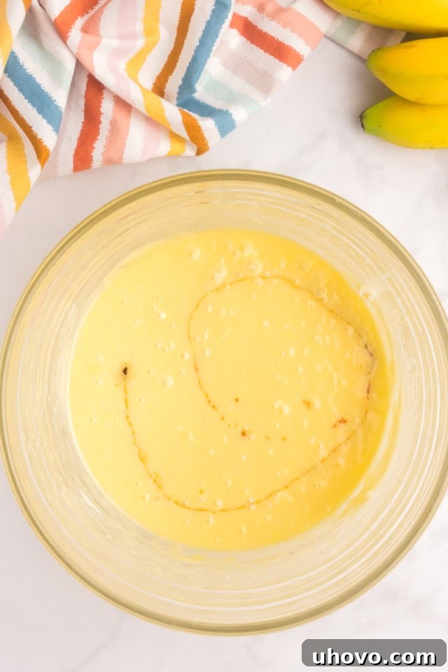 An overhead view of clear vanilla extract being added to a partially mixed cake batter in a glass bowl, enhancing its aroma.