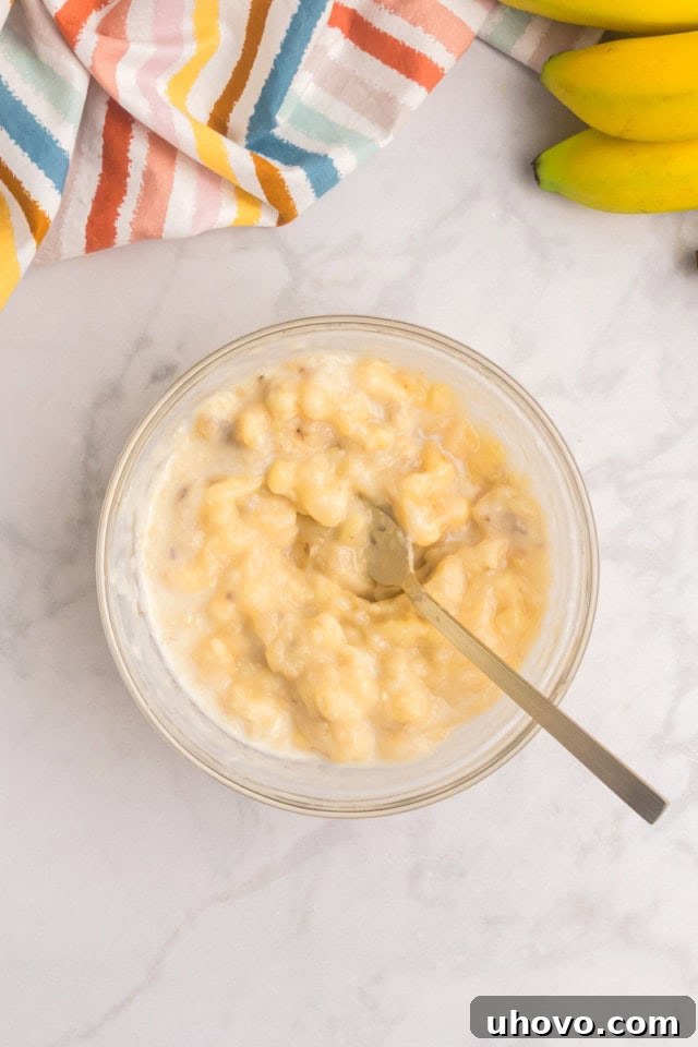 An overhead view of mashed ripe bananas combined with milk in a small bowl, creating a smooth, pourable mixture.