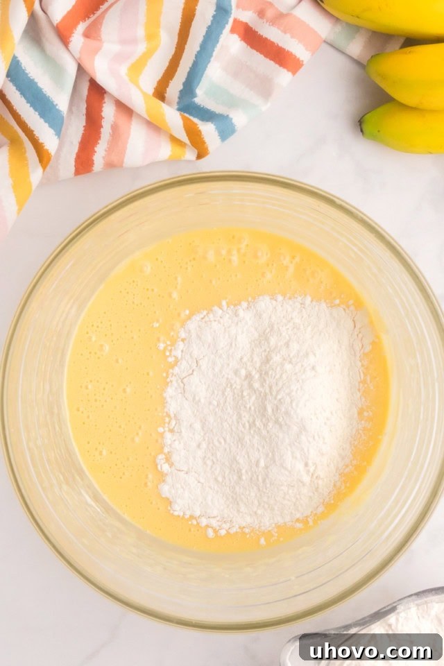 An overhead view of half of the dry flour mixture being added to the wet cake batter in a mixing bowl.