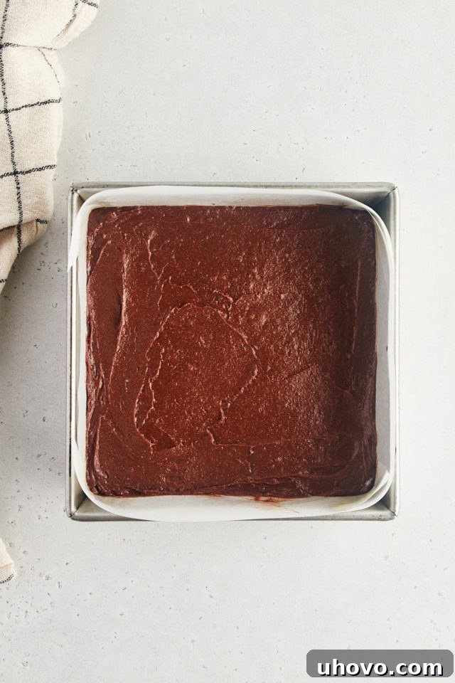 Overhead view of rich brownie batter spread evenly in a parchment-lined baking pan.