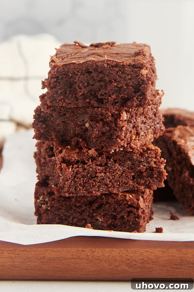 Stack of 4 fudgy brownies on parchment paper, showing their thick, gooey centers.