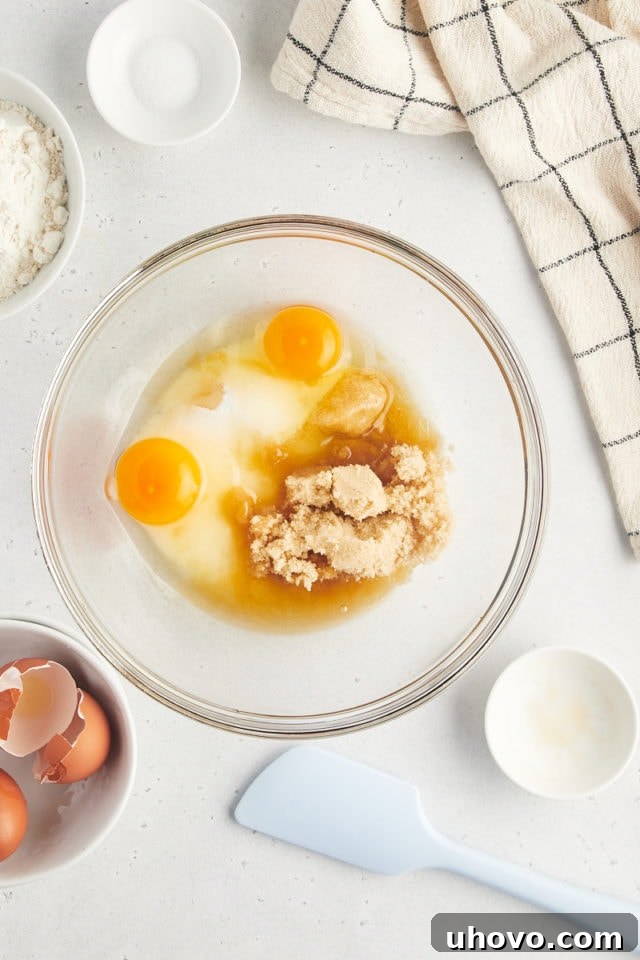 Overhead view of wet ingredients (sugars, eggs, vanilla) for brownies in a glass mixing bowl.
