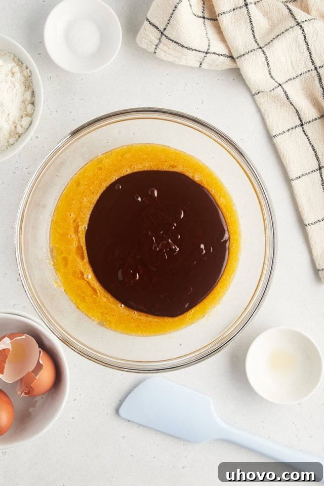 Overhead view of the melted chocolate mixture being added to the egg and sugar mixture in a glass bowl.