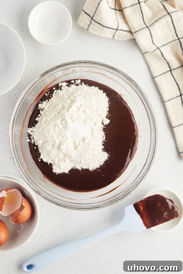 Overhead view of dry ingredients (flour and salt) being added to the wet and chocolate mixture for brownies.