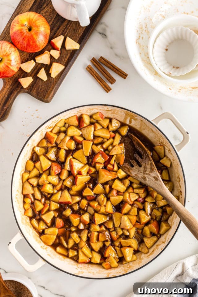 An overhead view of the bubbling, cooked apple cobbler filling simmering in a large pan on the stovetop, rich with brown sugar.