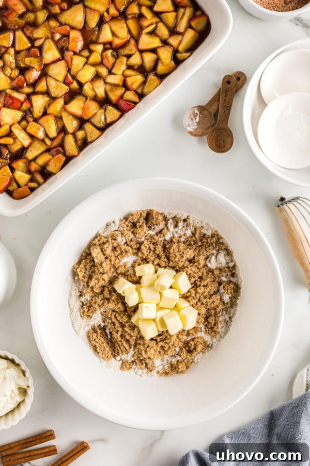An overhead view of the dry ingredients for the apple cobbler topping, with cold butter cubes, in a white mixing bowl, ready to be blended.