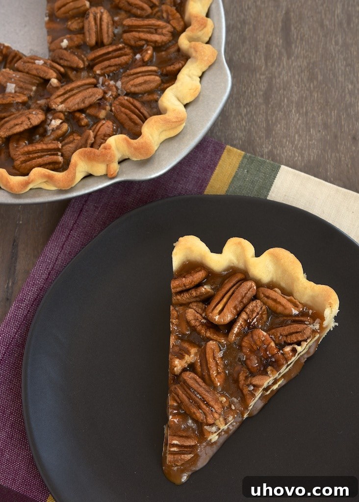 A generous slice of Salted Caramel Pecan Pie resting on a white plate, showcasing the distinct layers of flaky crust, crunchy pecans, and shimmering, gooey caramel filling.