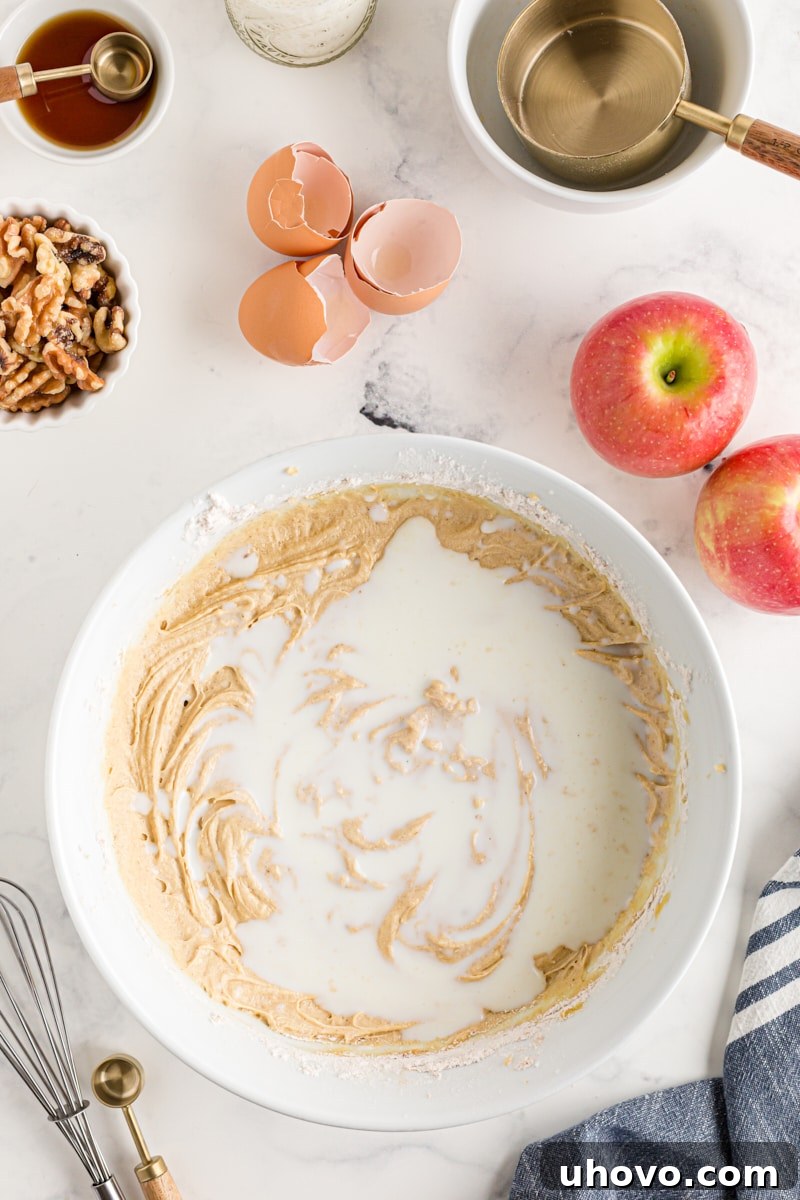 Overhead view of milk being added to the cake batter in a white mixing bowl during the alternating process
