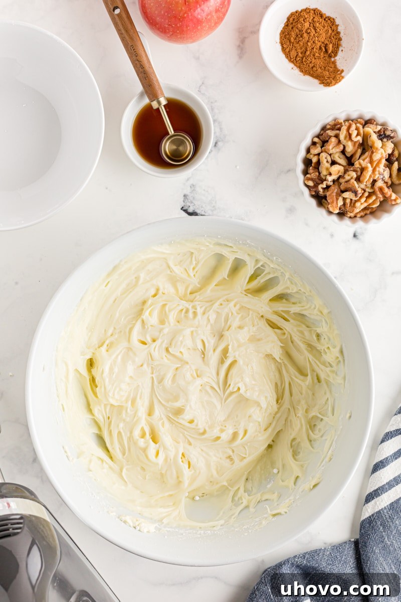 Overhead view of partially mixed cream cheese frosting in a white mixing bowl, with confectioners' sugar being incorporated