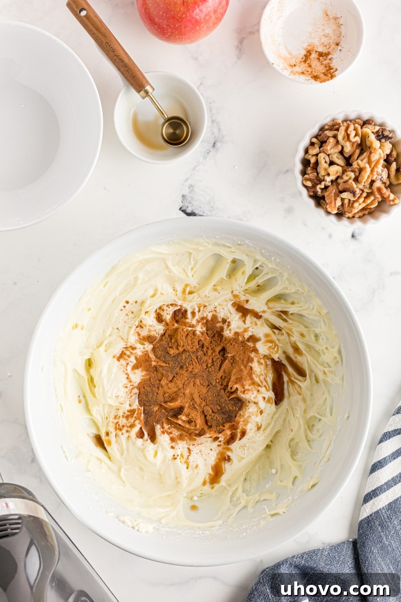 Overhead view of ground cinnamon being added to the smooth cream cheese frosting in a white mixing bowl