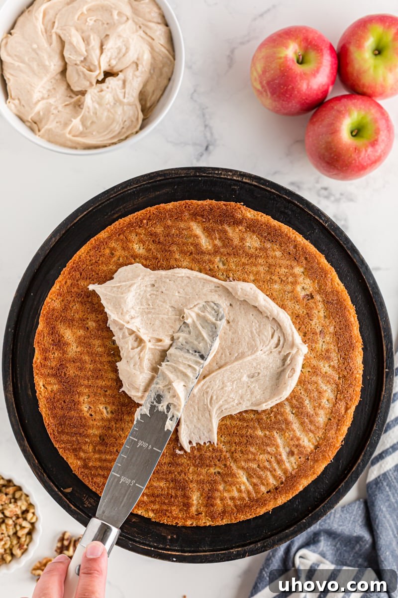 Overhead view of rich cinnamon cream cheese frosting being spread evenly onto an apple spice cake layer