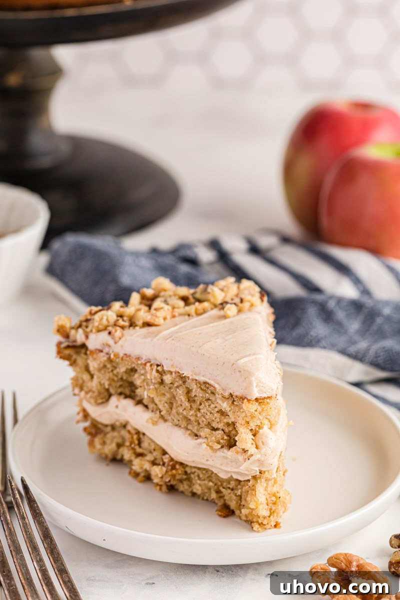 A delectable slice of apple spice cake with a generous dollop of cream cheese frosting on a pristine white cake plate