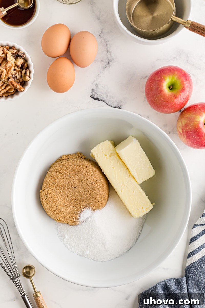 Overhead view of butter, granulated sugar, and brown sugar in a white mixing bowl, ready to be creamed