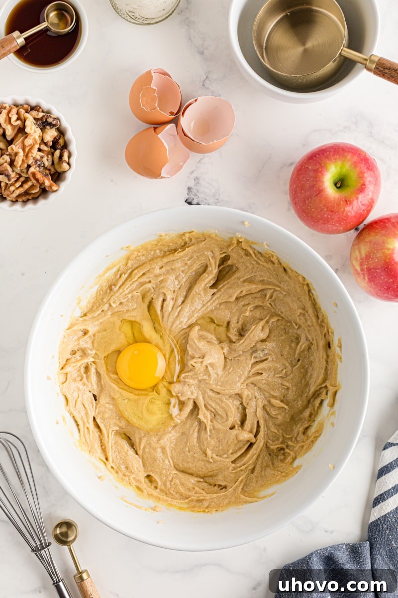 Overhead view of an egg being added to the creamed butter and sugar mixture for apple spice cake batter