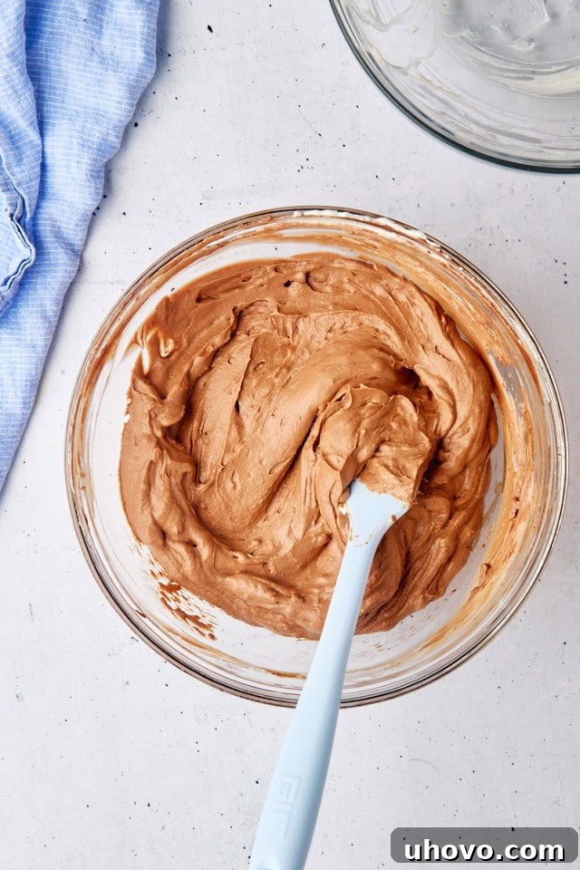 Close-up overhead view of the completed, smooth, and airy no-bake chocolate cheesecake batter in a clear glass bowl, showcasing its readiness for assembly.