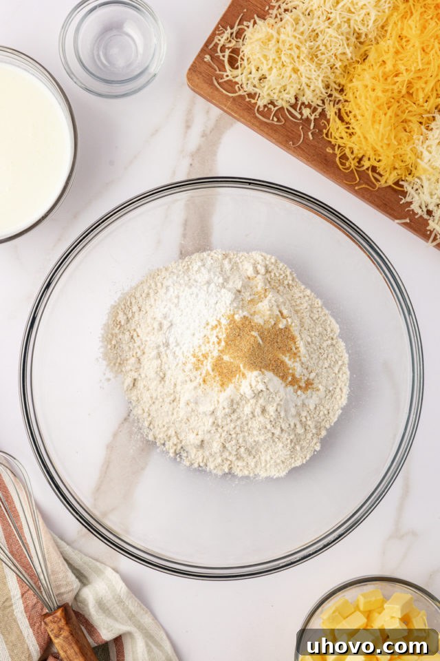 overhead view of all-purpose flour, baking powder, baking soda, salt, and garlic powder in a clear glass mixing bowl, perfectly measured and ready to be whisked