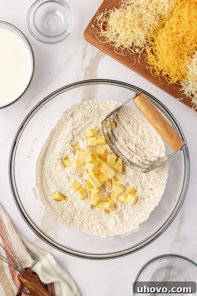 overhead view of cold cubed unsalted butter being added to the dry biscuit ingredients in a glass mixing bowl