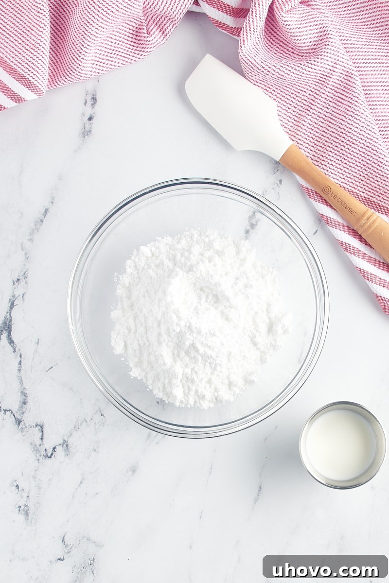 Powdered sugar in a glass bowl with a small cup of milk beside it, ready to be mixed into a glaze.