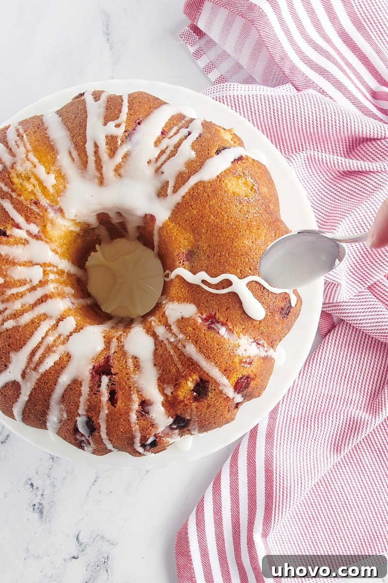 Spoonfuls of white glaze being drizzled over the top of the cooled Cranberry Bundt Cake.