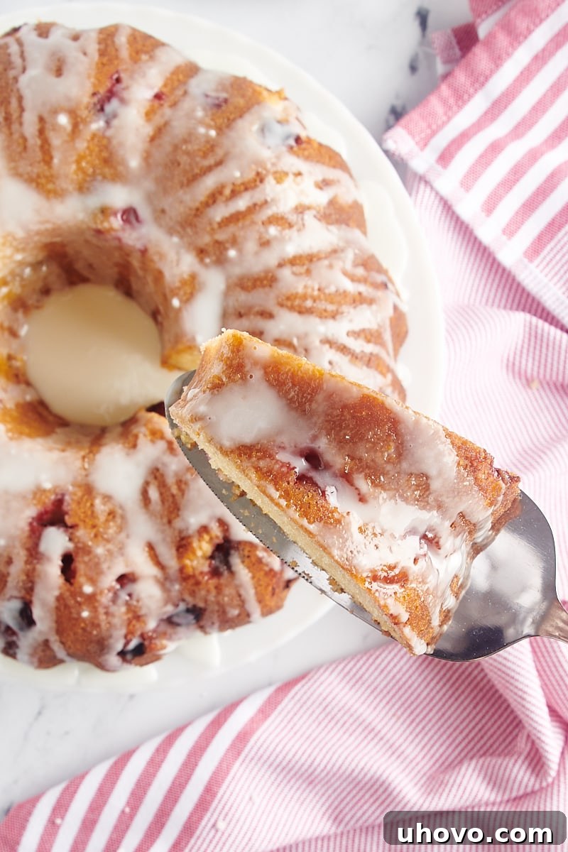 A hand reaching in to take a perfectly sliced piece of the glazed Cranberry Bundt Cake from the platter.