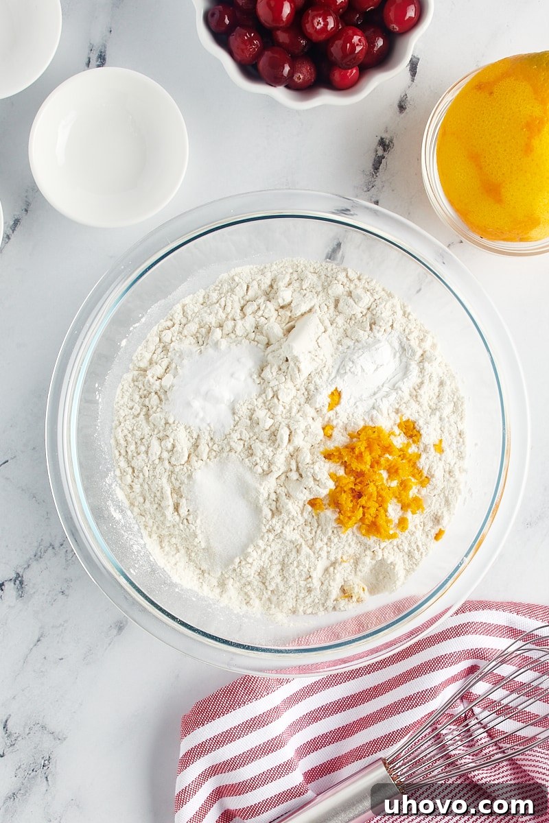 Mixing dry ingredients in a glass bowl, including flour, baking powder, baking soda, salt, and orange zest.