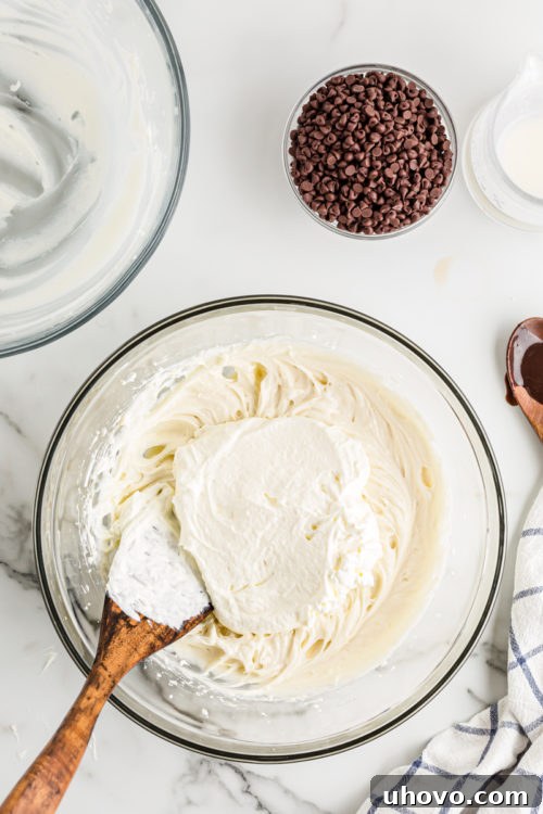 The gentle process of folding freshly whipped cream into the rich cream cheese mixture, ensuring a light and airy cheesecake filling.