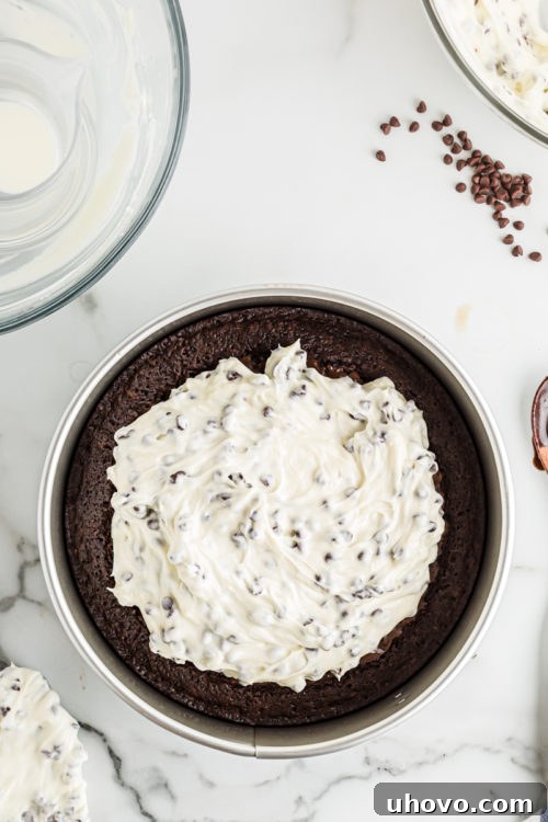 A generous dollop of creamy cheesecake mixture placed atop the cooled brownie crust, poised for spreading.