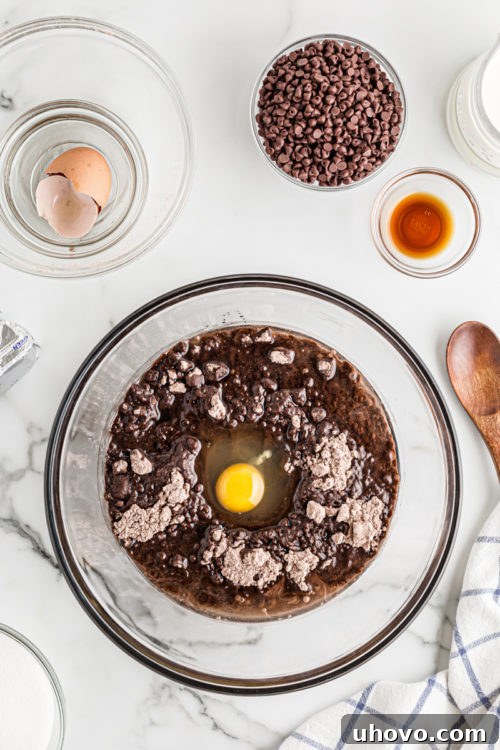 An egg cracked into a bowl of rich brownie batter, illustrating the initial mixing stage for the brownie crust.
