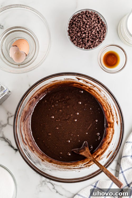 Smooth, glossy brownie batter resting in a clear glass mixing bowl, perfectly prepared for baking into the crust.