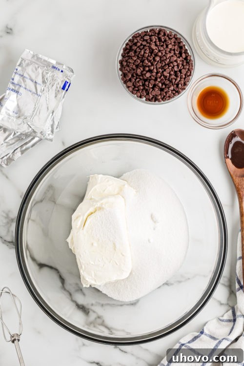Softened cream cheese and granulated sugar combined in a clear glass mixing bowl, poised for whipping into a creamy cheesecake base.
