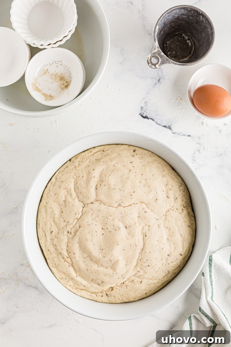 Herb cloverleaf dinner roll dough significantly expanded and risen in a bowl, coated with cooking spray.