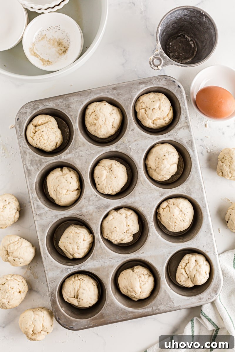Divided portions of dinner roll dough placed into the cups of a muffin tin, ready for shaping into cloverleaf rolls.