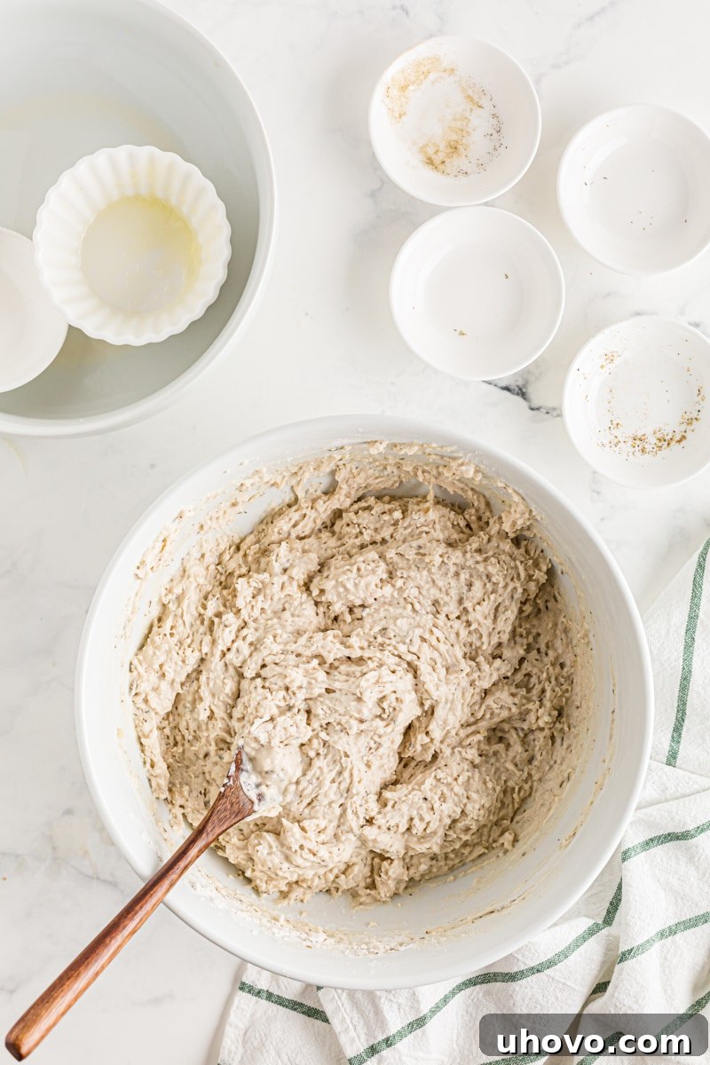 The bread dough being mixed thoroughly with a sturdy wooden spoon in a bowl.