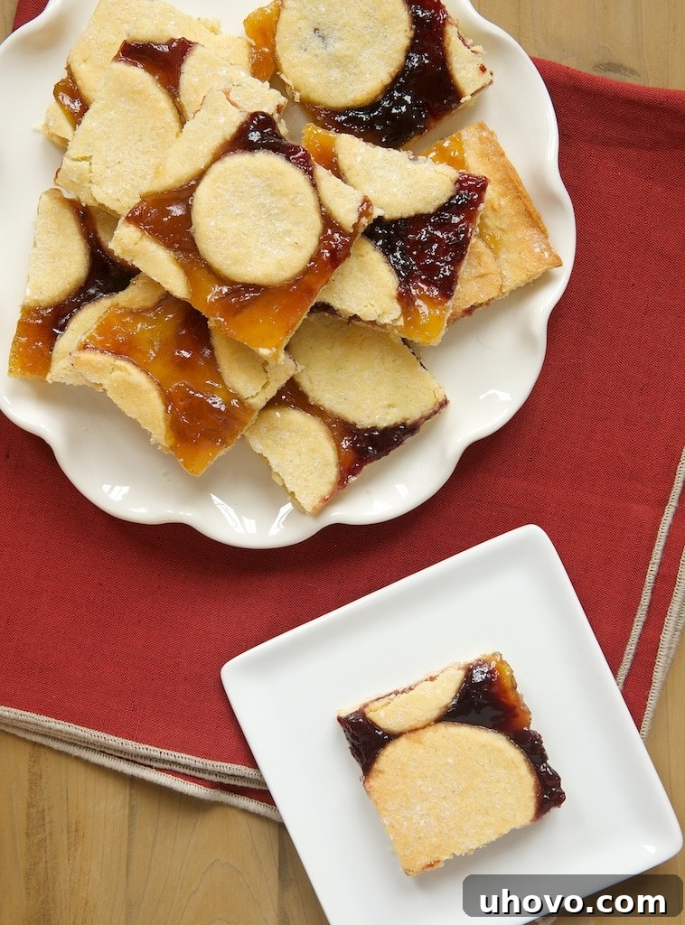 Close-up of baked Linzer Bars, showcasing the golden crust and the vibrant fruit preserve filling with decorative dough cutouts.