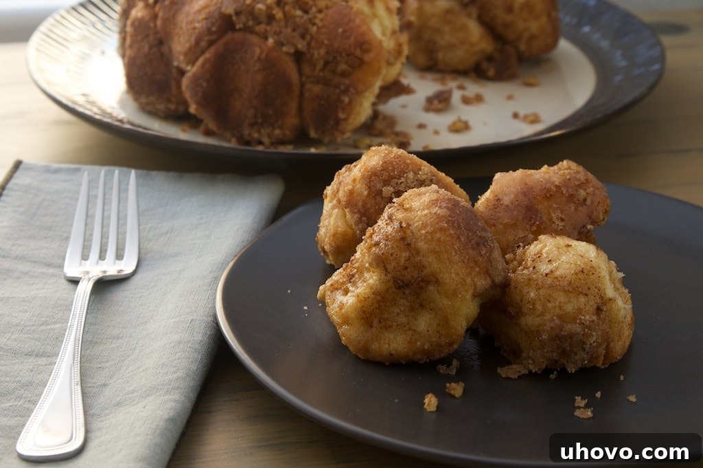 four pieces of brown butter cinnamon pull apart bread on a dark gray plate with more bread in the background