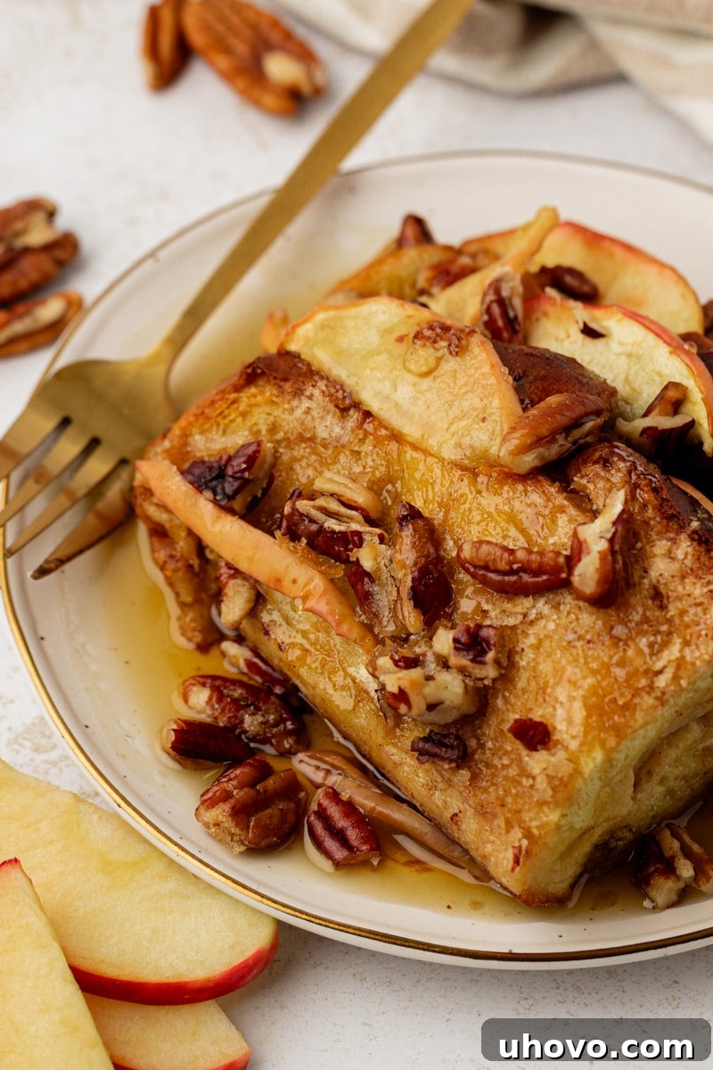Plate of apple cinnamon baked French toast with a generous drizzle of maple syrup and chopped pecans, ready to be enjoyed.