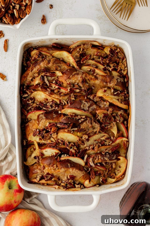 A freshly baked pan of golden-brown apple cinnamon baked French toast, with caramelized apples and pecans on top, cooling after baking.