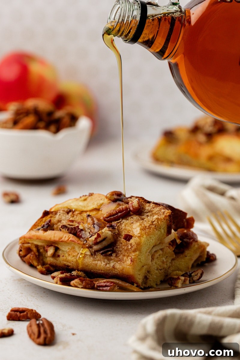 A stream of rich, golden maple syrup being poured gracefully onto a plate showcasing a slice of warm apple cinnamon baked French toast, highlighting its inviting texture.