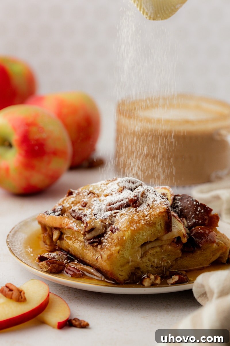 A delicate dusting of confectioners' sugar descends onto a warm, golden slice of apple cinnamon French toast, adding a sweet and elegant finish.
