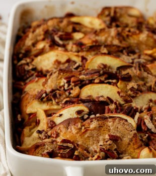 A golden-brown baking dish brimming with apple cinnamon baked French toast, caramelized apples, and toasted pecans.