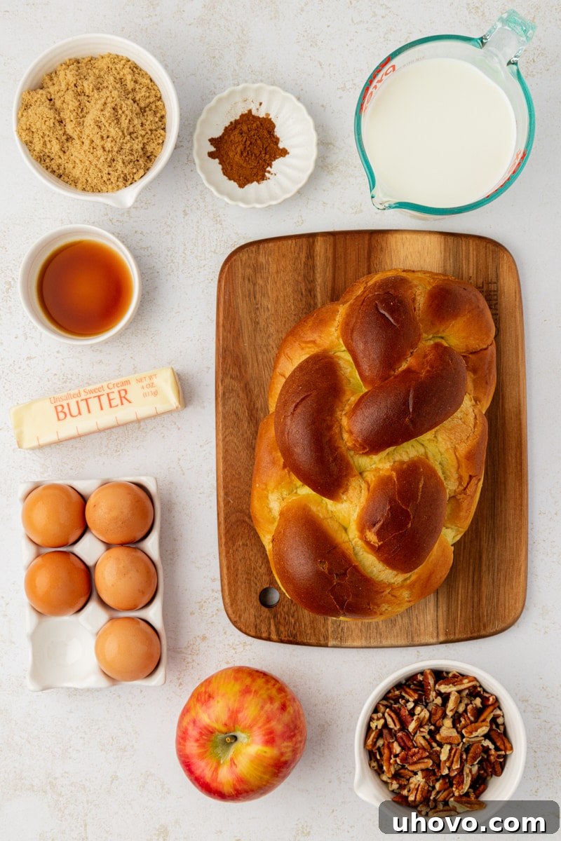 Overhead view displaying all the fresh, high-quality ingredients laid out for preparing apple cinnamon baked French toast, including challah bread, apples, pecans, and spices.