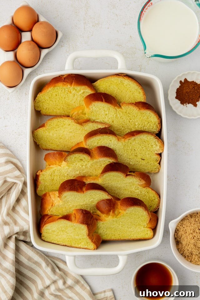 Overhead view of challah bread slices neatly arranged in a baking dish, preparing for the French toast custard.