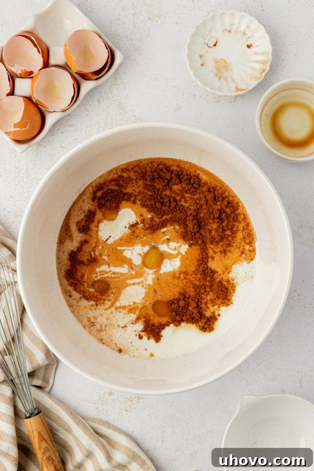 Overhead shot of eggs, milk, brown sugar, cinnamon, and vanilla in a mixing bowl, prior to being whisked into a smooth custard.