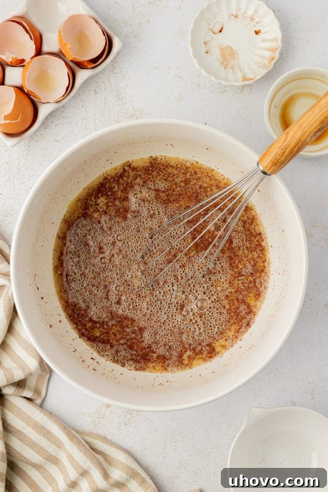 A whisk swirls through a creamy, golden custard mixture in a bowl, perfectly combined and ready for the French toast.
