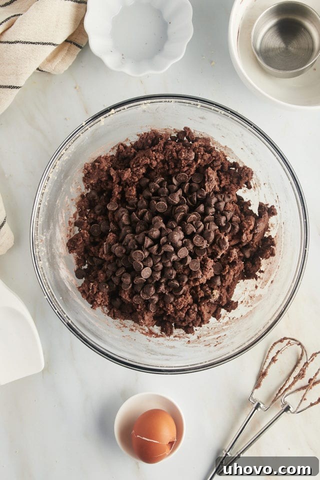 Overhead view of chocolate chips added to mixing bowl with dough