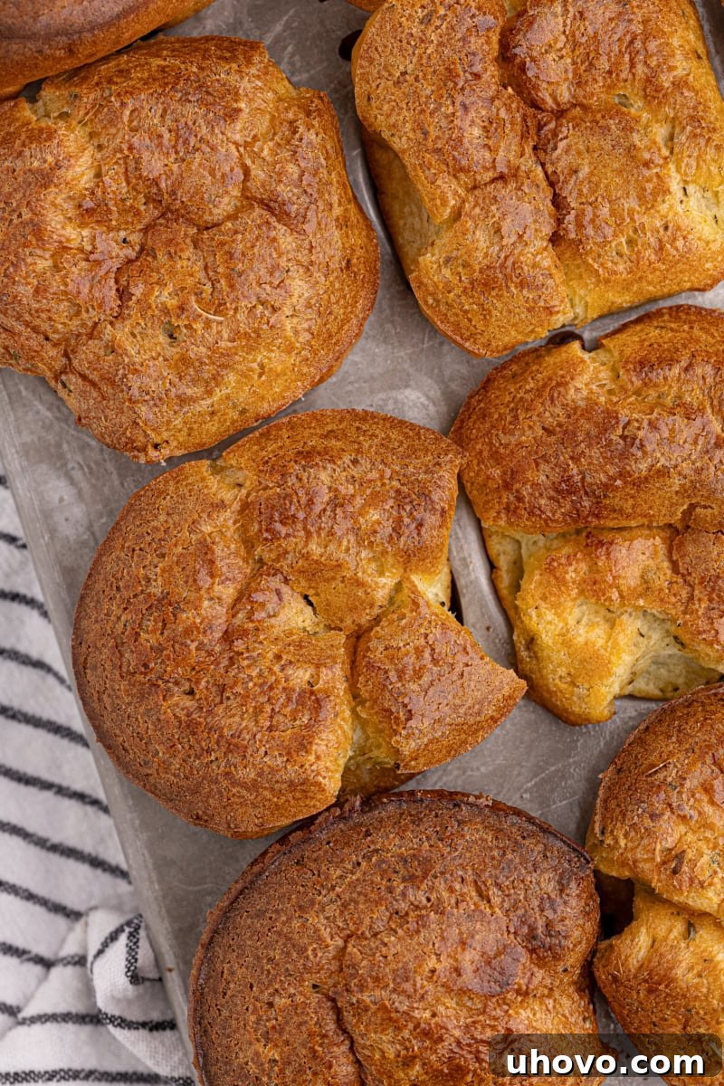 Close-up view of three freshly baked, perfectly puffed popovers still nestled in a standard muffin pan.
