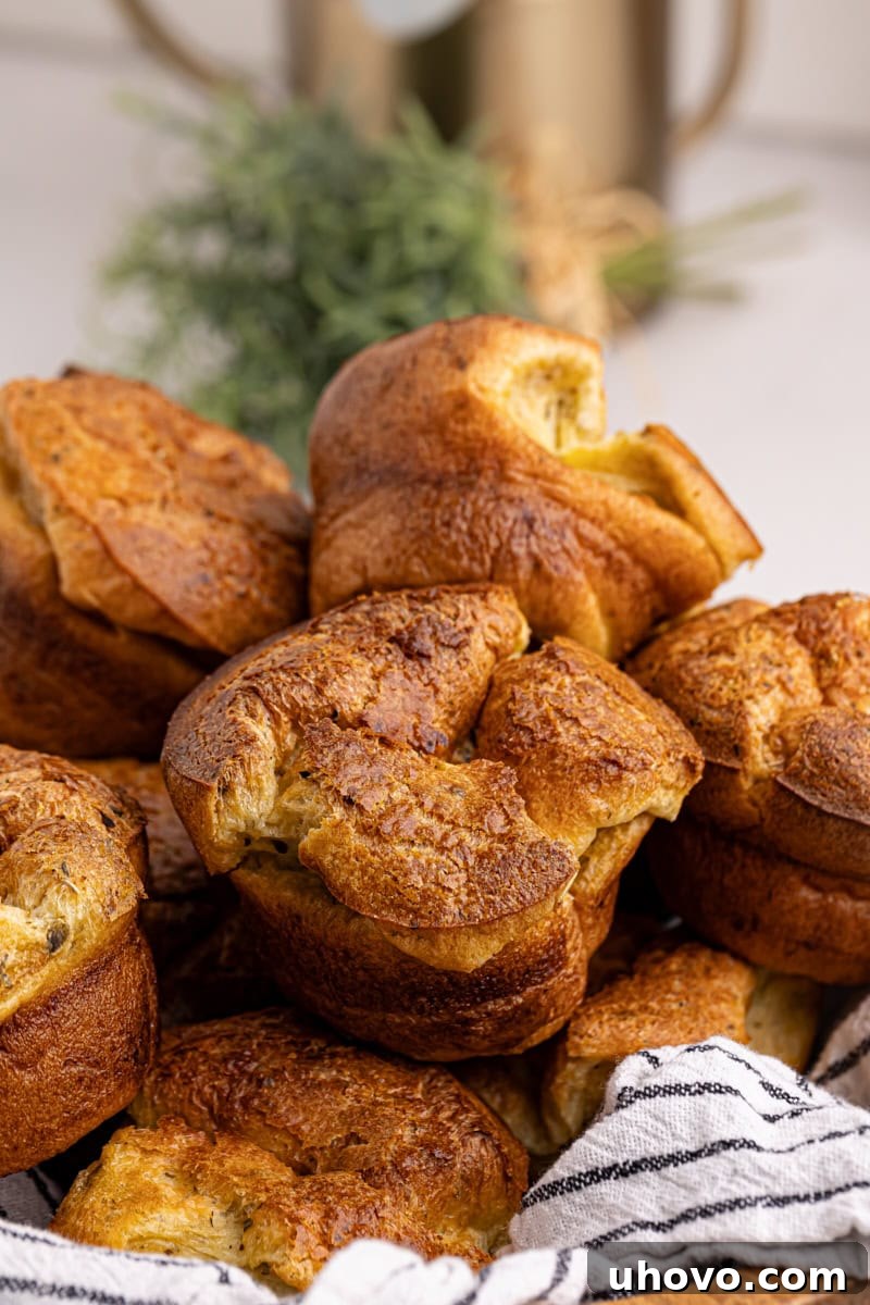 A wooden bowl filled with freshly baked popovers, lined with a striped towel, showcasing their golden color and airy texture.